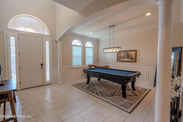 entrance foyer featuring billiards, arched walkways, ornamental molding, a decorative wall, and ornate columns