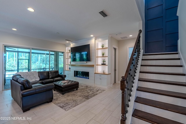 living area with wood tiled floor, visible vents, stairway, a glass covered fireplace, and recessed lighting