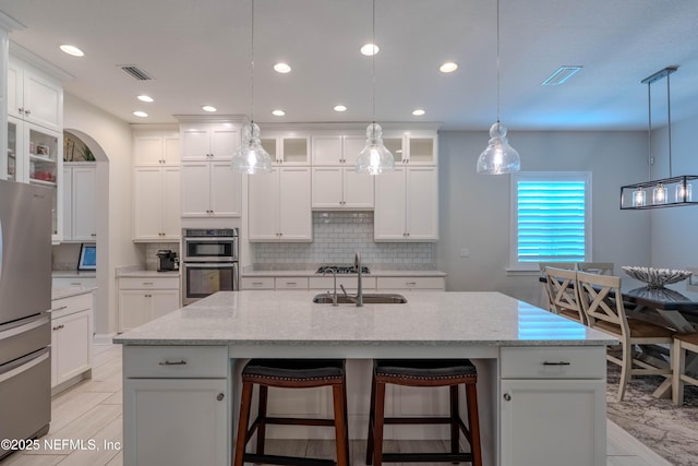 kitchen featuring an island with sink, white cabinetry, a sink, appliances with stainless steel finishes, and backsplash