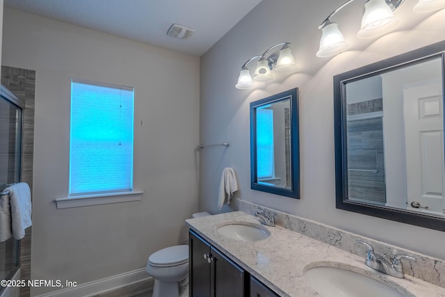 full bath featuring a sink, a shower with shower door, toilet, and double vanity