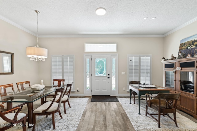 foyer featuring crown molding, light wood-style flooring, a textured ceiling, a notable chandelier, and baseboards