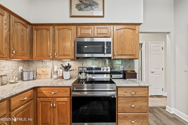kitchen with tasteful backsplash, light stone countertops, wood finished floors, and stainless steel appliances