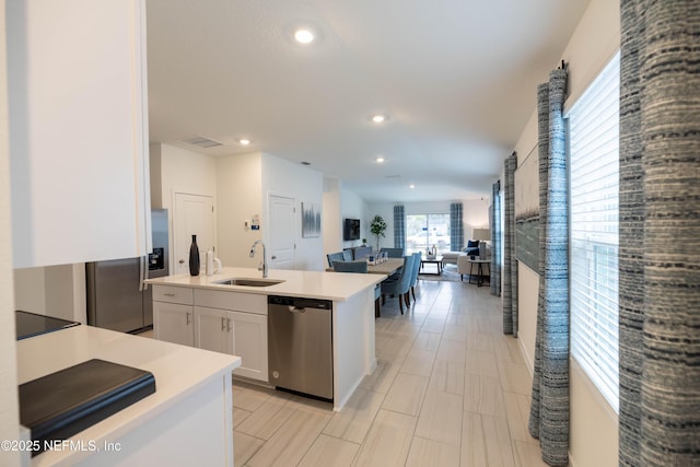 kitchen with white cabinetry, appliances with stainless steel finishes, light countertops, a sink, and open floor plan