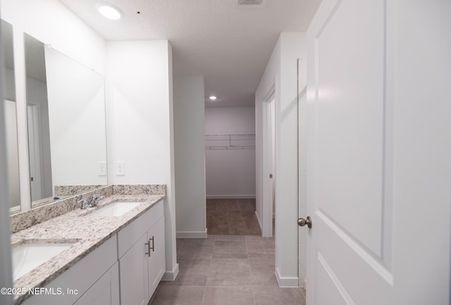 bathroom with tile patterned flooring, a sink, a walk in closet, double vanity, and baseboards