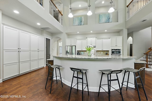 kitchen featuring visible vents, arched walkways, a high ceiling, appliances with stainless steel finishes, and dark wood-style floors