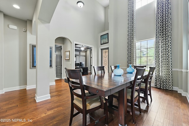 dining room featuring baseboards, a high ceiling, ceiling fan, arched walkways, and wood-type flooring
