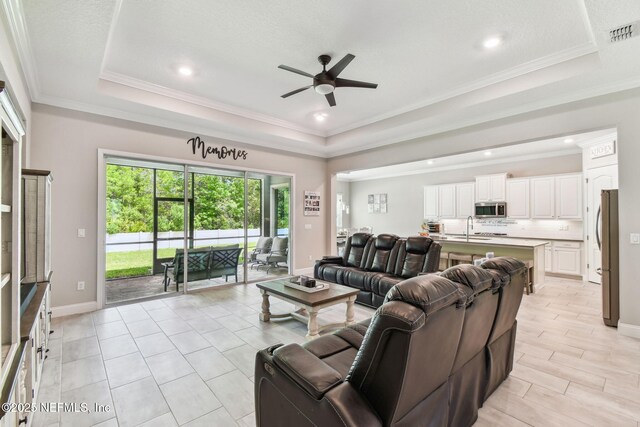 living area featuring a raised ceiling, crown molding, ceiling fan, and visible vents