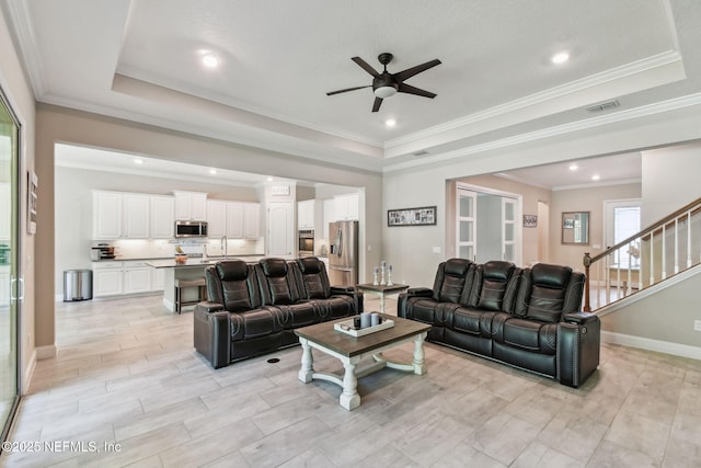 living area with visible vents, ceiling fan, baseboards, and a raised ceiling