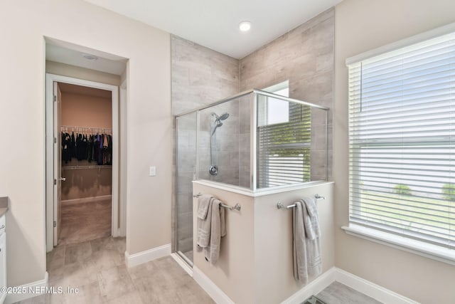 bathroom featuring a shower stall, vanity, baseboards, and a walk in closet