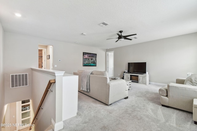living area featuring baseboards, carpet flooring, a textured ceiling, a ceiling fan, and visible vents