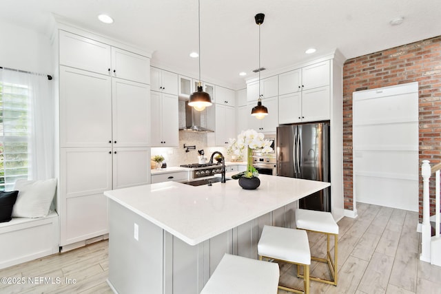 258 Haas Ave, Saint Augustine, FL 32095 - kitchen with appliances with stainless steel finishes, wall chimney exhaust hood, light wood-type flooring, white cabinetry, and brick wall