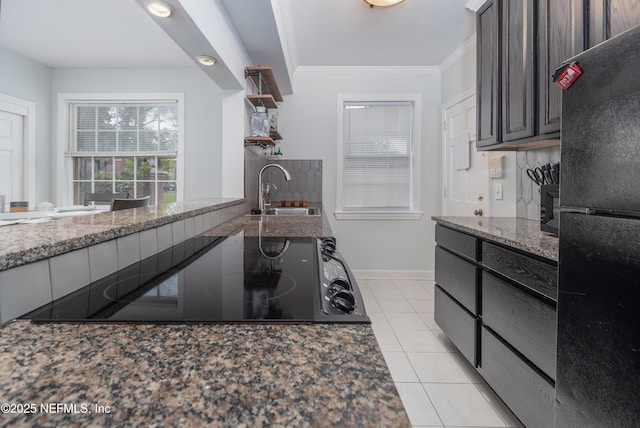 kitchen with dark stone countertops, a sink, crown molding, black appliances, and light tile patterned flooring