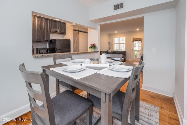 dining area with light wood-style floors, baseboards, visible vents, and a barn door