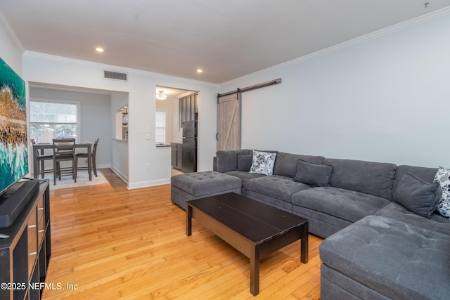 living room with crown molding, visible vents, light wood-style flooring, and a barn door
