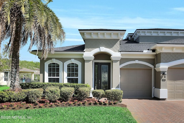 mediterranean / spanish home featuring roof with shingles, decorative driveway, a garage, and stucco siding