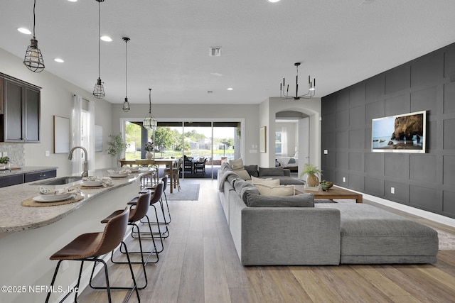 living area with arched walkways, light wood finished floors, visible vents, and recessed lighting