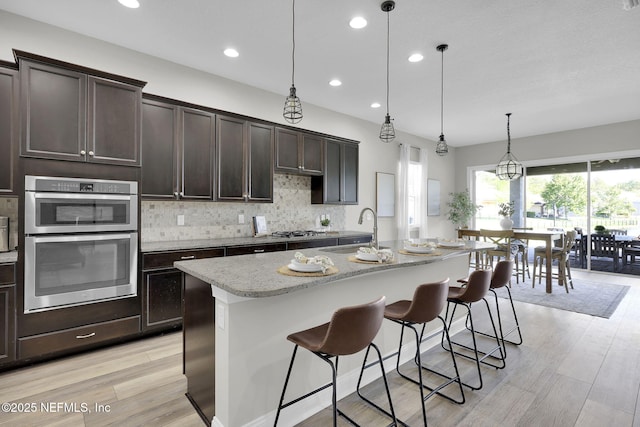 kitchen with tasteful backsplash, a sink, appliances with stainless steel finishes, light wood-style floors, and a kitchen bar