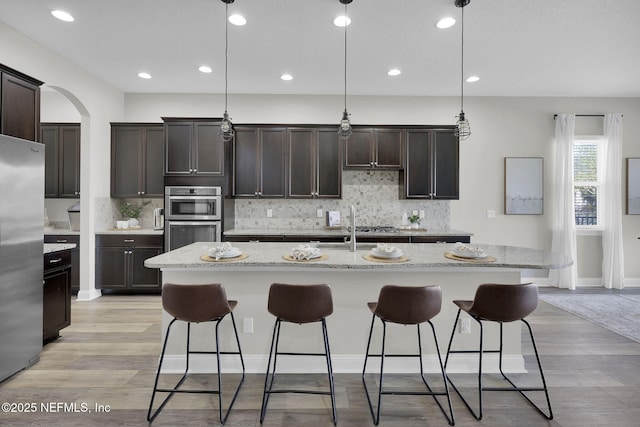 kitchen with appliances with stainless steel finishes, light wood-style floors, a kitchen bar, dark brown cabinets, and decorative backsplash