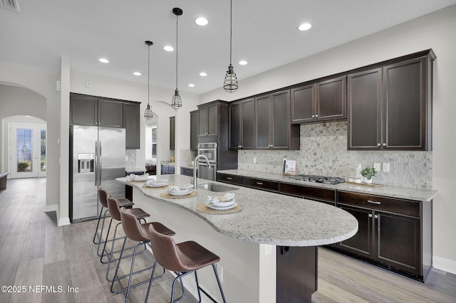 kitchen featuring light wood-type flooring, dark brown cabinets, appliances with stainless steel finishes, arched walkways, and a sink