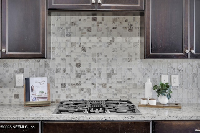 kitchen with light stone countertops, dark brown cabinetry, stainless steel gas cooktop, and backsplash