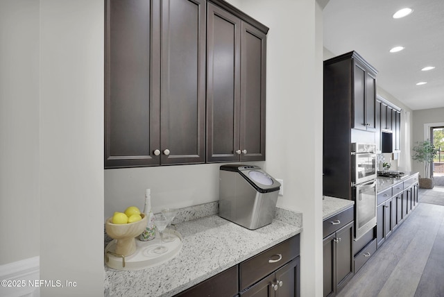 kitchen with light wood-style floors, dark brown cabinets, light stone countertops, and recessed lighting