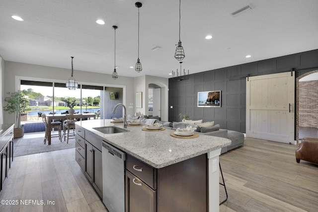 kitchen featuring open floor plan, stainless steel dishwasher, a sink, and light wood finished floors