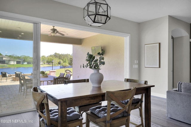 dining area featuring baseboards, a ceiling fan, a water view, arched walkways, and wood finished floors