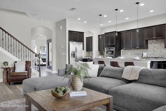 living area featuring recessed lighting, arched walkways, light wood-style floors, and visible vents