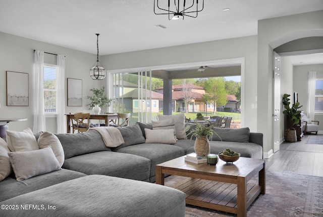 living area with a notable chandelier, baseboards, visible vents, arched walkways, and wood finished floors