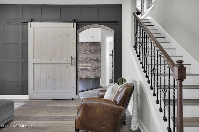 entryway featuring arched walkways, a decorative wall, stairway, and wood finished floors