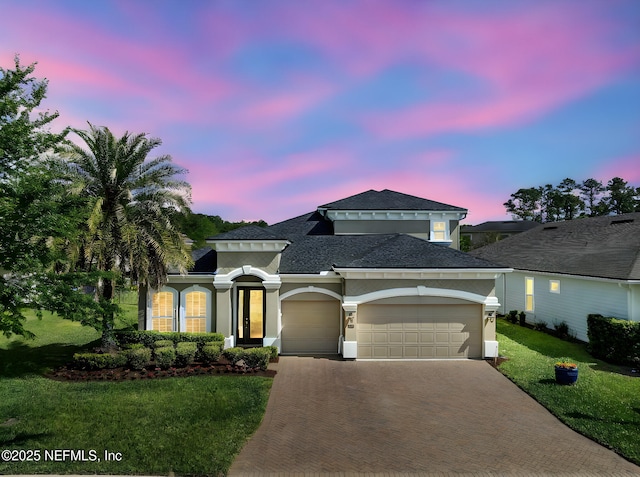 view of front facade with a front yard, a garage, stucco siding, decorative driveway, and roof with shingles