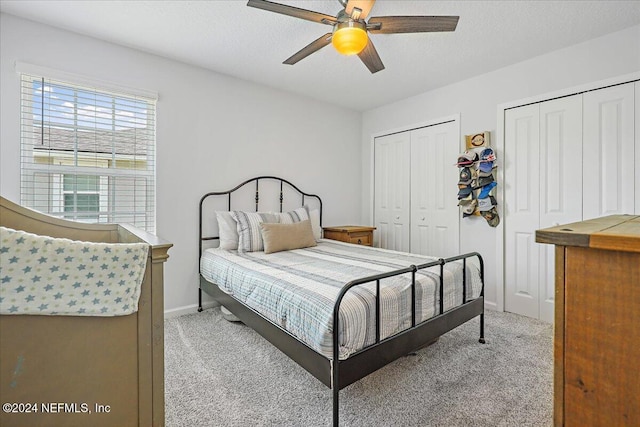 bedroom featuring baseboards, light colored carpet, multiple closets, and ceiling fan