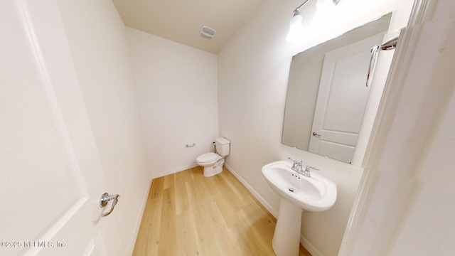 half bathroom with visible vents, toilet, wood finished floors, and baseboards