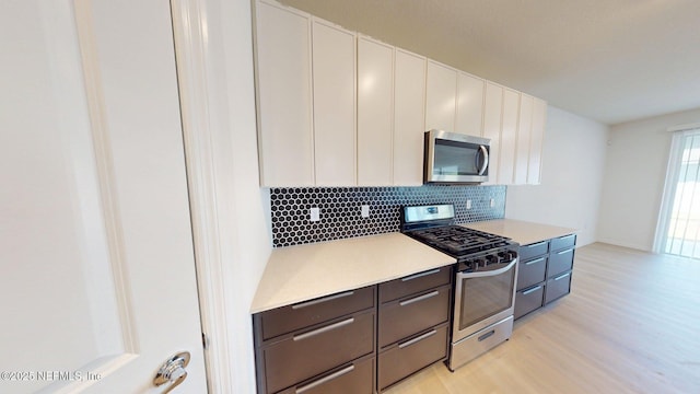 kitchen with light countertops, backsplash, white cabinets, stainless steel appliances, and light wood finished floors