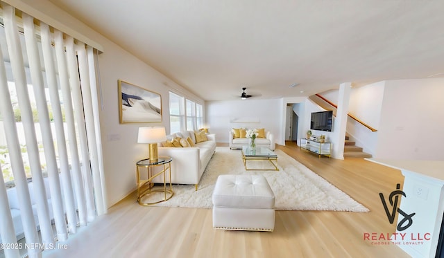 living area with stairway, a ceiling fan, and wood finished floors