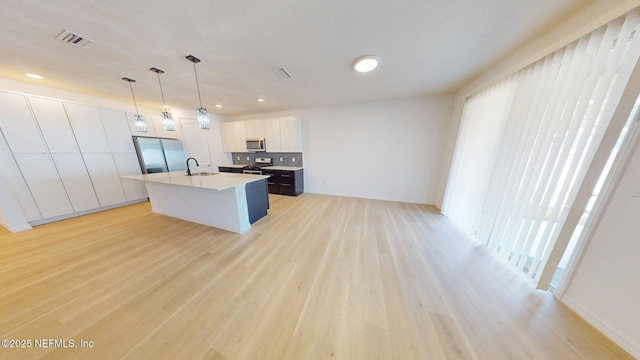 kitchen with an island with sink, light countertops, visible vents, appliances with stainless steel finishes, and a sink
