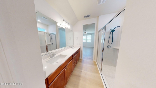 full bathroom featuring visible vents, a sink, a shower stall, double vanity, and wood finished floors