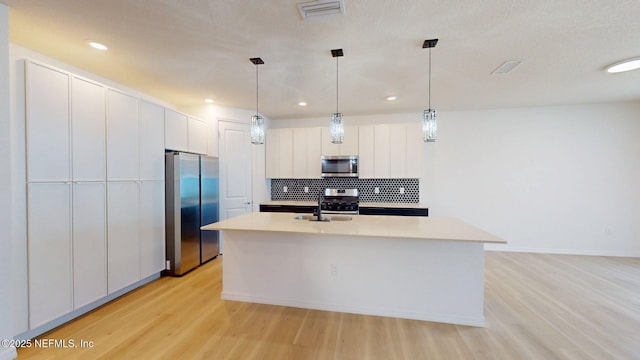 kitchen featuring tasteful backsplash, light countertops, light wood-style floors, a center island with sink, and stainless steel appliances