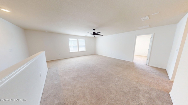 unfurnished room with a textured ceiling, a ceiling fan, visible vents, light carpet, and baseboards