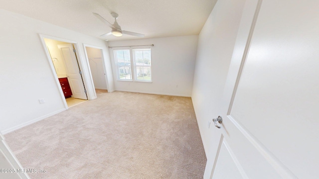 unfurnished bedroom with a closet, ceiling fan, a walk in closet, ensuite bath, and light carpet