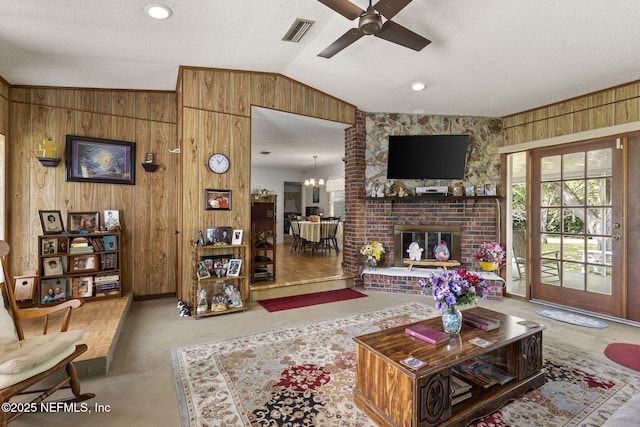 living room featuring visible vents, a fireplace, ceiling fan with notable chandelier, wood walls, and lofted ceiling