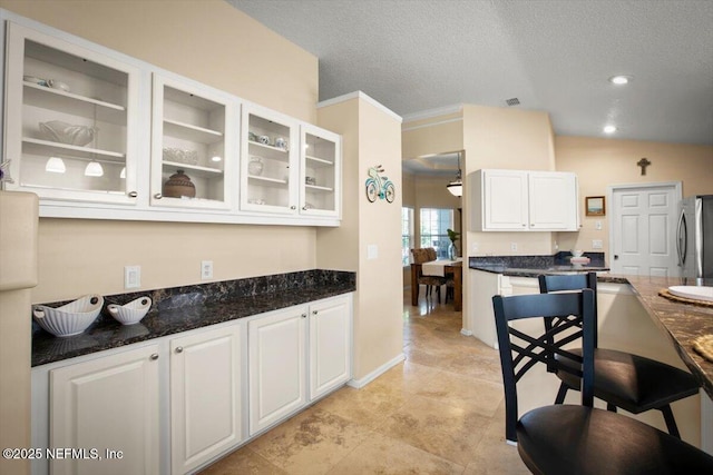 1886 Mourning Dove Ln, Jacksonville Beach, FL 32250 - kitchen with freestanding refrigerator, white cabinetry, glass insert cabinets, a textured ceiling, and dark stone counters
