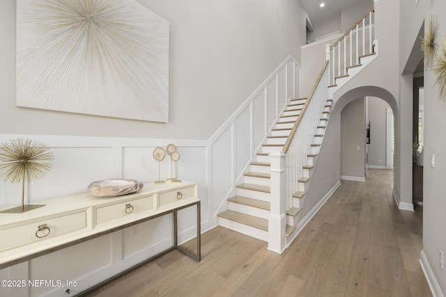 247 Vale Dr, Saint Augustine, FL 32095 - staircase with arched walkways, baseboards, a high ceiling, wood finished floors, and a decorative wall