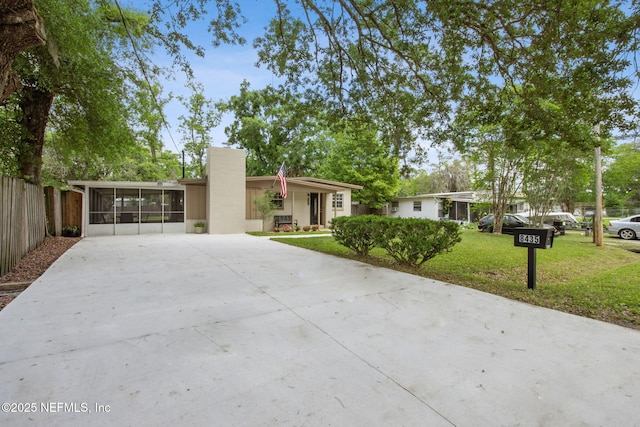view of front facade featuring a sunroom, concrete driveway, a front yard, and fence