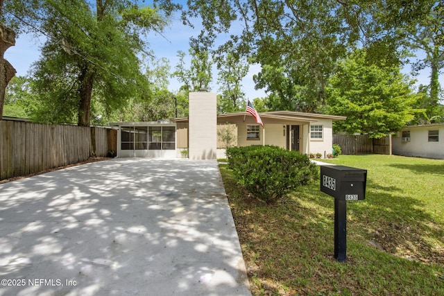view of front of property with a sunroom, concrete driveway, fence, and a front lawn