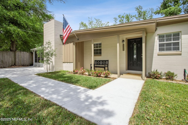 view of exterior entry featuring a yard, concrete block siding, and fence