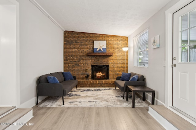 interior space with light wood-style flooring, a textured ceiling, a brick fireplace, lofted ceiling, and baseboards