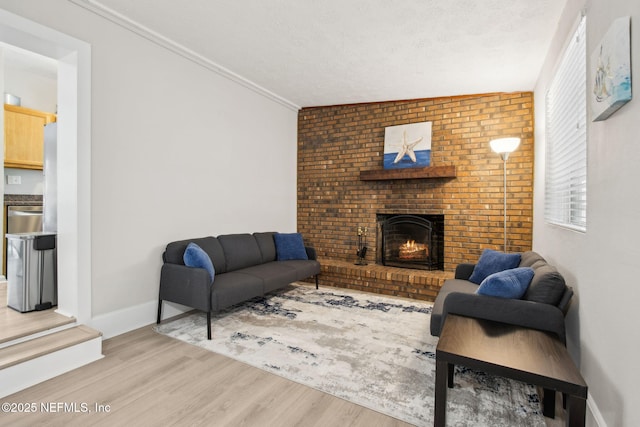 living area featuring a fireplace, a textured ceiling, ornamental molding, wood finished floors, and baseboards