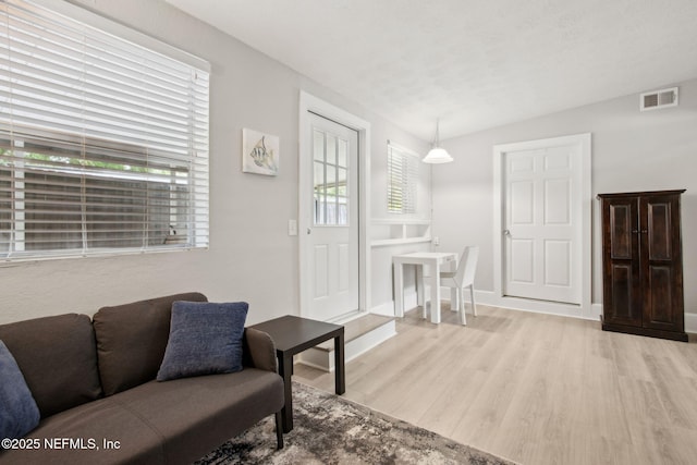 living area featuring visible vents, plenty of natural light, vaulted ceiling, and light wood-style floors