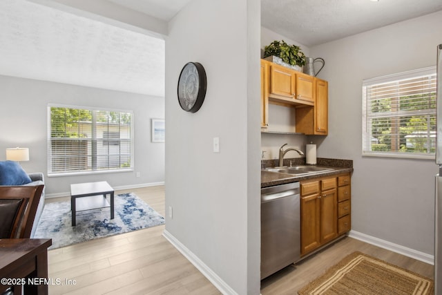kitchen with light wood-type flooring, open floor plan, dark countertops, stainless steel dishwasher, and a sink